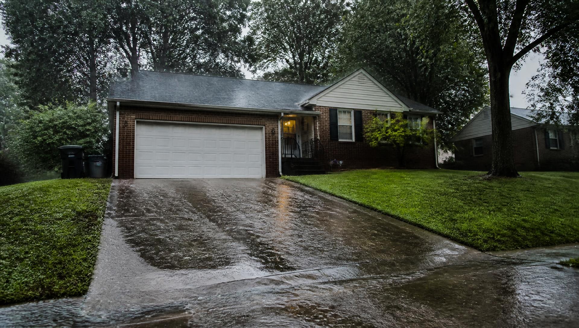 Rain sheeting down a sloped residential driveway toward a garage in Birmingham, Alabama